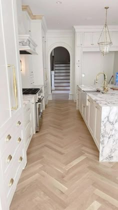 a large kitchen with white cabinets and marble counter tops, along with herringbone wood flooring