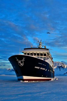 a large boat floating on top of a snow covered ocean under a cloudy blue sky