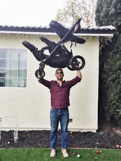 a man standing in front of a house holding up an upside down car sculpture