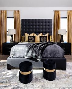 a bedroom with black and gold decor, including a large bed in front of two windows