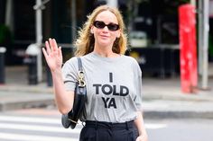 a woman in grey shirt and black pants walking down street with her hand out to the side