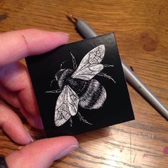 a hand holding a small black and white drawing of a bee on a piece of paper