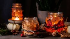 three jars filled with candles sitting on top of a table next to small pumpkins