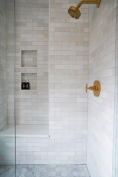 a white tiled shower with gold fixtures and shelves on the wall, along with marble flooring