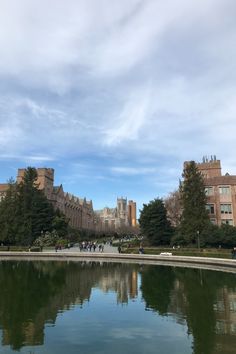 a pond in the middle of a park with buildings on both sides and people walking around it