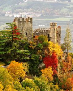 an old castle on top of a hill surrounded by trees with autumn foliage around it