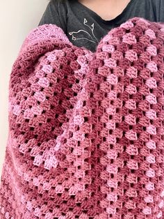 a pink crocheted blanket sitting on top of a white wall next to a woman's face