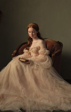 a woman in a dress sitting on a chair holding a book and looking at the camera