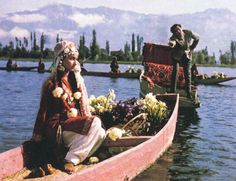 a man sitting in a boat on top of a lake next to another person with flowers