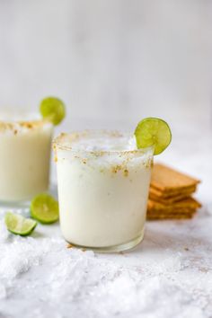 two glasses filled with drinks and garnished with limes on the rim, sitting on snow