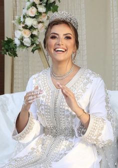 a woman wearing a tiara sitting on top of a white couch next to a flower arrangement