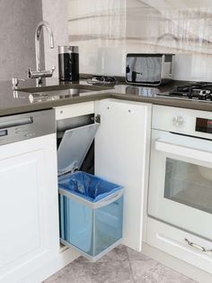 a kitchen with white cabinets and gray counter tops, an open trash can in the corner