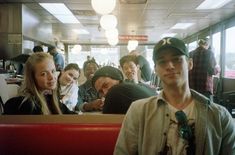 a group of people sitting in a booth at a fast food restaurant, some with hats on