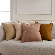 four different colored pillows sitting on top of a couch in front of a white wall