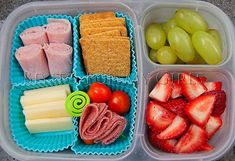 two plastic containers filled with food on top of a table next to grapes, strawberries and crackers