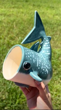 a hand holding a blue ceramic fish cup in it's left hand, with grass in the background