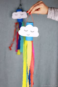 a hand holding a paper cloud with eyes and rainbow streamers hanging from it's side