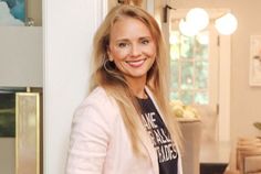 a woman with long blonde hair standing in front of a door smiling at the camera