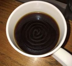 a white cup filled with liquid sitting on top of a wooden table