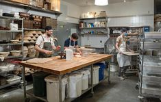 three people working in a large kitchen with lots of shelves and pans on the counter