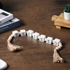 the word blessing spelled with cubes and tassels on a wooden table next to a computer mouse