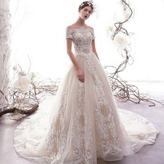 a woman in a wedding dress standing on a white floor with flowers and branches around her