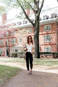 a woman standing in front of a red brick building with trees and grass around her