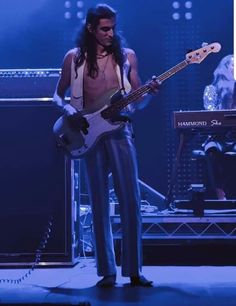 a man with long hair and no shirt playing a bass guitar in front of an audience