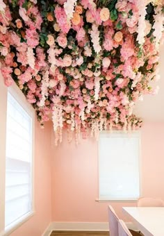 a room with pink walls and flowers hanging from the ceiling over the desks in front of the window