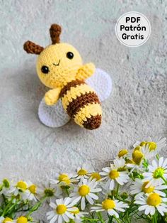 a crocheted bee sitting next to some daisies