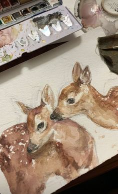 a painting of two baby deers sitting on top of a table next to a paintbrush