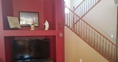 a living room with red walls and a tv on the wall next to a stair case