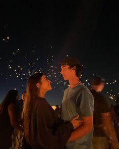 two people standing next to each other with fireworks in the sky