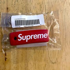 a red supreme keychain sitting on top of a wooden table next to a plastic bag