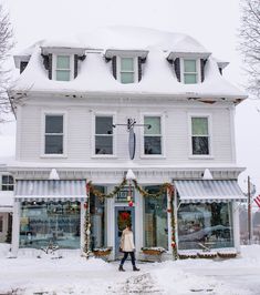 a woman walking in front of a white building covered in snow