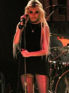 a woman with long blonde hair is holding a microphone and standing in front of a drum set