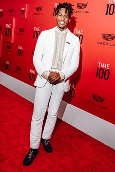 a man in a white suit standing on a red carpet with his hands in his pockets