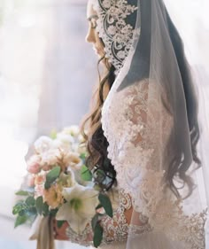 a woman in a wedding dress holding a bouquet with flowers on the side and veil over her head