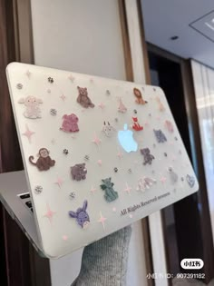 an apple laptop with many different stickers on it's cover, in front of a window