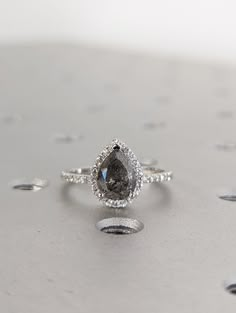 an engagement ring with a pear shaped diamond surrounded by small white and black dots on a gray surface