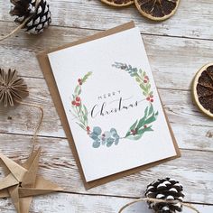 a christmas card sitting on top of a wooden table next to dried oranges and pine cones