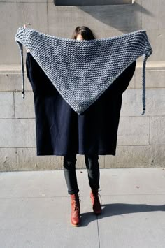 a woman is standing on the sidewalk with a shawl draped over her head