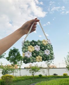 a hand is holding a small green and white flower ornament hanging from a string