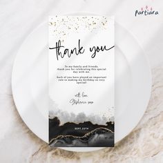 a white plate with a black and gold foiled thank you card on top of it