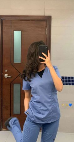 a woman in scrubs taking a selfie with her cell phone while standing in front of a door