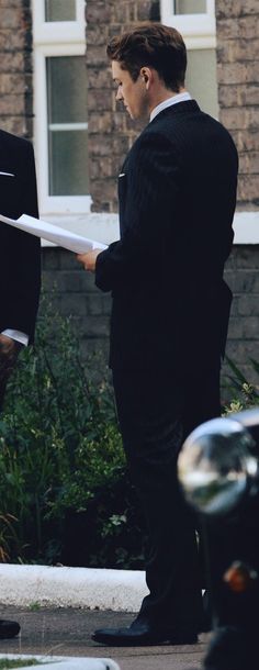 a man in a suit and tie holding papers while standing next to a motorcycle on the street