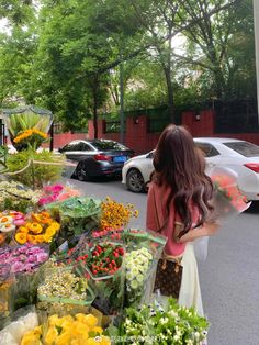 a woman standing in front of a bunch of flowers on the side of a road