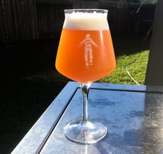 a glass filled with liquid sitting on top of a table next to a grass covered yard