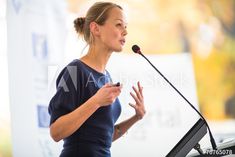 a woman standing at a podium with a microphone in front of her and speaking into a microphone