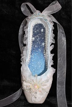 a ballerina shoe with white lace and blue glitters on the bottom, tied to a satin ribbon